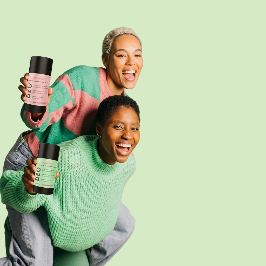 Two smiling people pose together against a solid green studio background, each holding a bottle of Nubar DEO. One person wears a pink and mint sweater, and the other wears a mint green sweater.